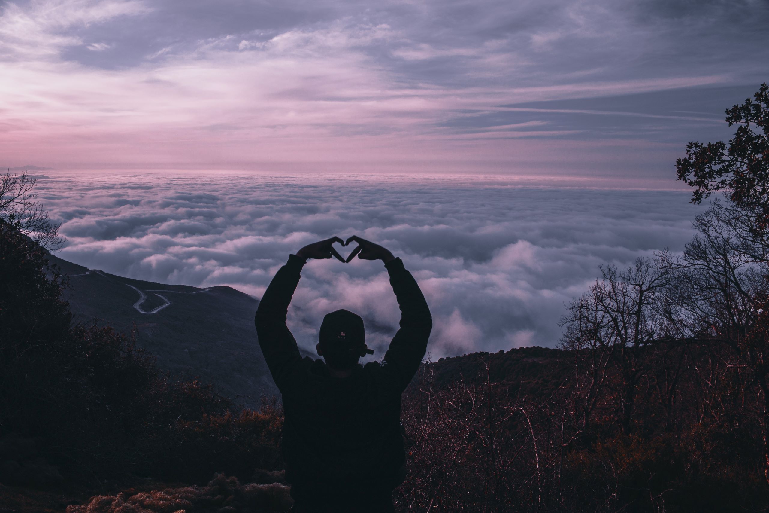 Person making a heart shape with hands on a mountain top to show they love the view